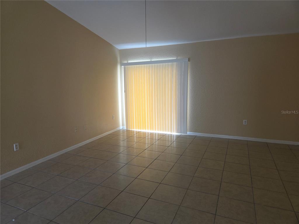 An empty room features beige walls, light-colored tile flooring, and a sliding glass door — 8 SAWFISH COURT, POINCIANA, FL