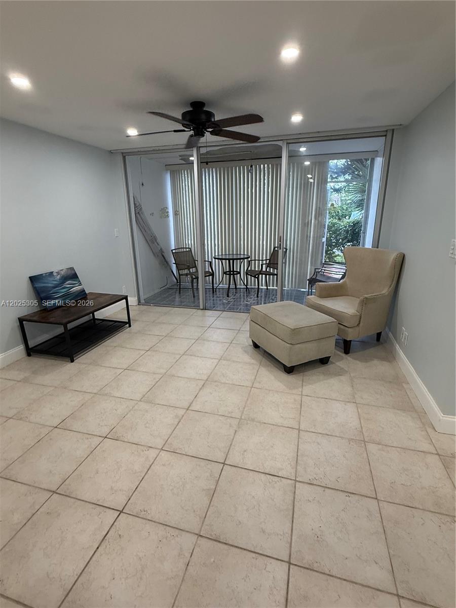 A living room features light tile flooring, a ceiling fan, and sliding doors to a patio — 942 NE 199th St # 102, Miami FL 33179, MIAMI, FL