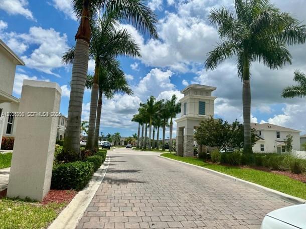 A paved road leads through a residential entrance with palm trees and stone pillars — 754 SE 19th St, Homestead FL 33034, HOMESTEAD, FL