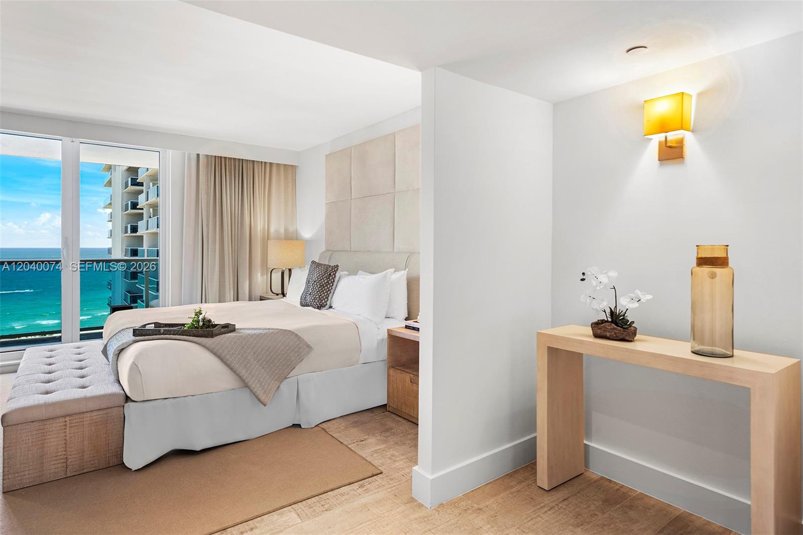 A bedroom features a bed with a tufted bench, ocean views, and a console table — 102 24 # 1222, Miami Beach FL 33139, MIAMI BEACH, FL