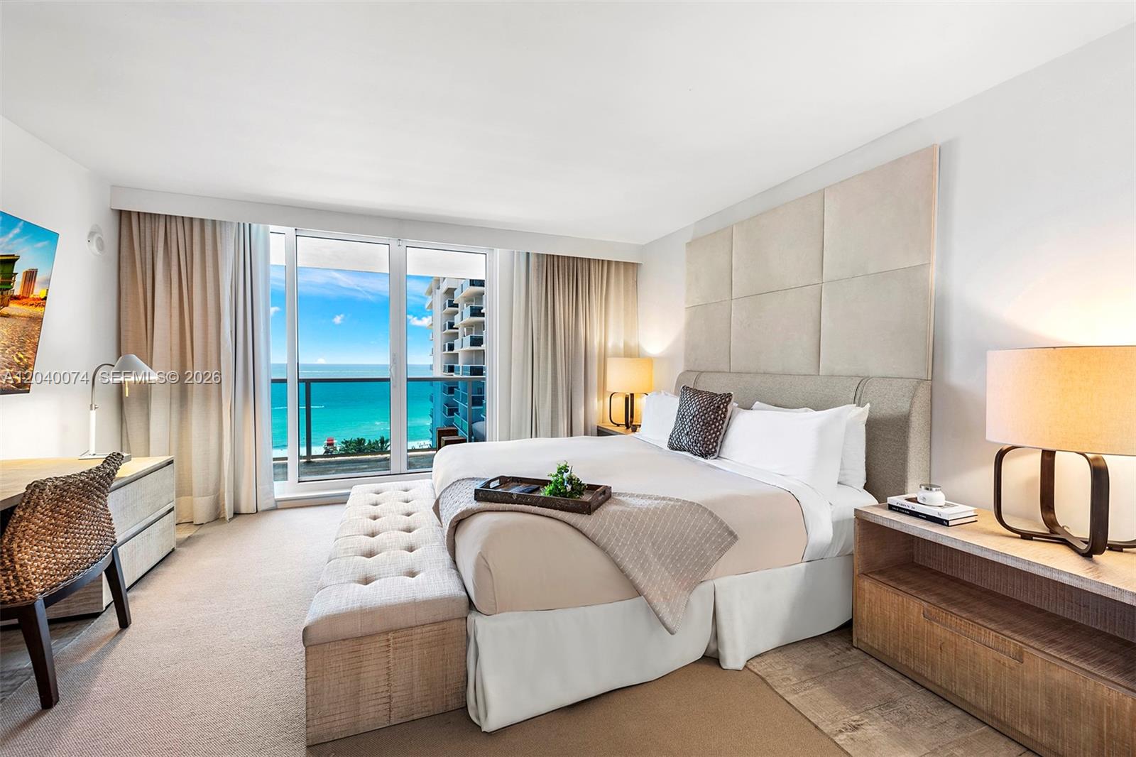 A bedroom features a king bed, tufted bench, desk, and a balcony with ocean views — 102 24 # 1222, Miami Beach FL 33139, MIAMI BEACH, FL