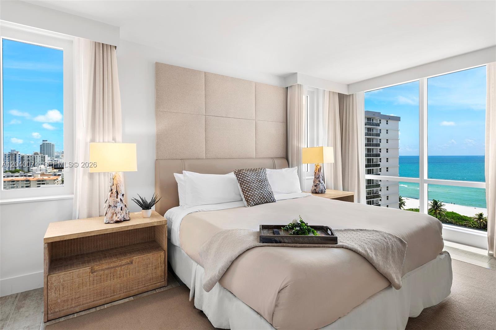 A bedroom features a bed with a beige headboard, two lamps, and ocean views — 102 24 # 1222, Miami Beach FL 33139, MIAMI BEACH, FL