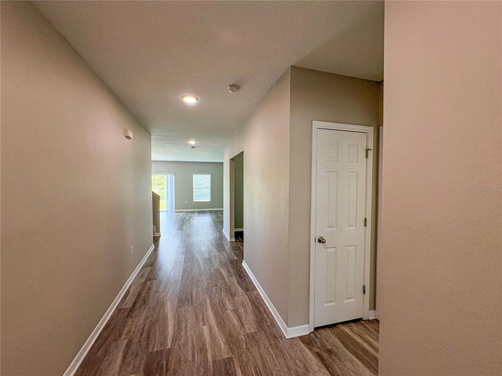 A hallway with wood-look flooring leads toward a living area with a sliding glass door — 4381 PUMICE DRIVE, LAKELAND, FL
