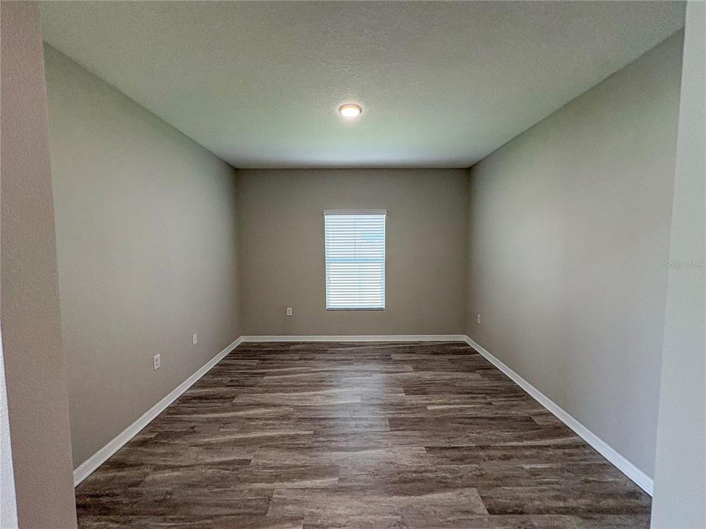 An empty room features light gray walls, a single window with blinds, and wood-look flooring — 4381 PUMICE DRIVE, LAKELAND, FL