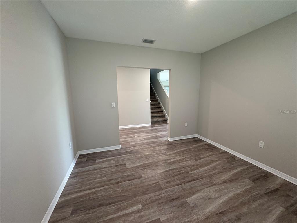 An empty room with gray walls and wood-look flooring leads to a staircase — 4381 PUMICE DRIVE, LAKELAND, FL