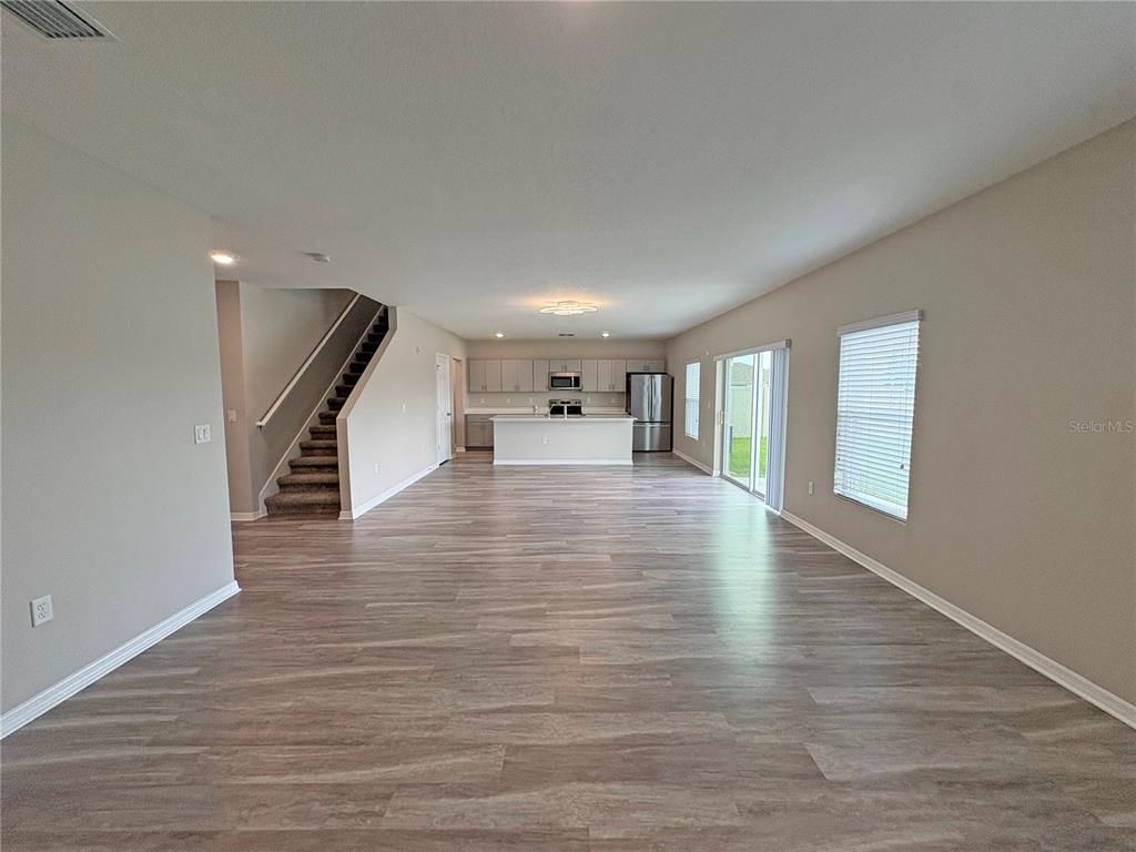 An open-concept living area features wood-look flooring, a staircase, and a kitchen with stainless appliances — 4381 PUMICE DRIVE, LAKELAND, FL