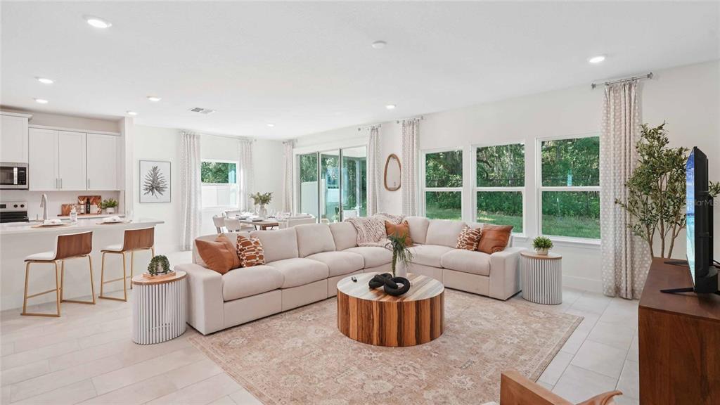 A bright open-concept living room features a large sectional sofa, wood coffee table, and kitchen — 11207 DUCKLING WAY, WEEKI WACHEE, FL