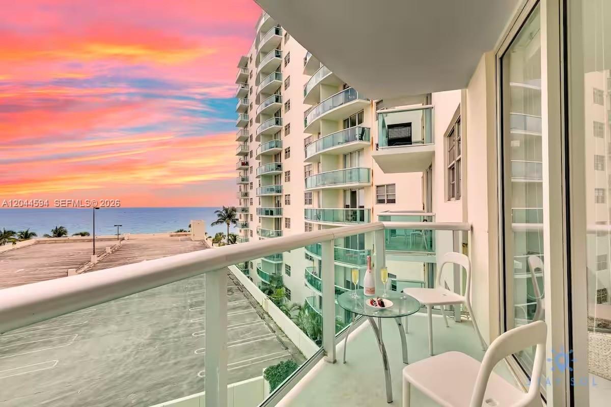 A balcony with a glass table and chairs overlooks a parking lot and the ocean — 3901 S Ocean Dr # 6Y, Hollywood FL 33019, HOLLYWOOD, FL