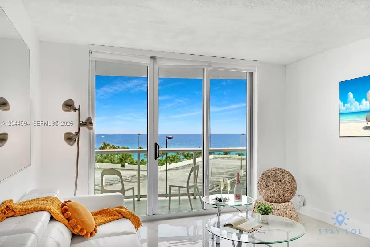 A bright living room features a white sofa, glass coffee tables, and sliding doors overlooking the ocean — 3901 S Ocean Dr # 6Y, Hollywood FL 33019, HOLLYWOOD, FL