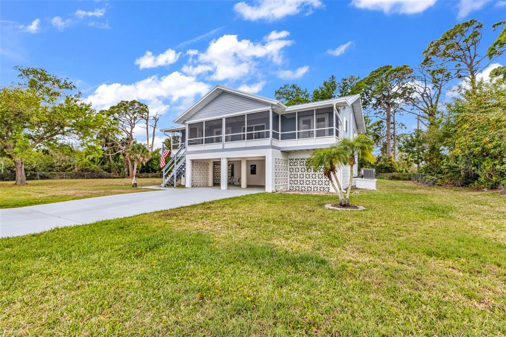 A stilt house with a screened porch, concrete driveway, and lattice skirting on a lawn — 3059 HOLCOMB ROAD, PORT CHARLOTTE, FL