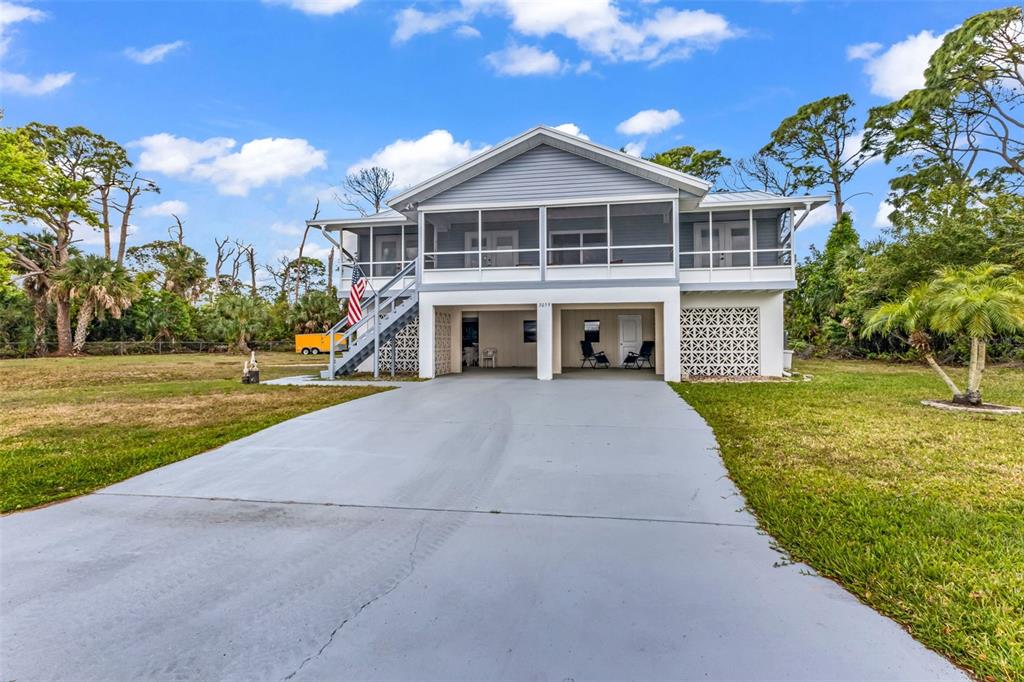 A two-story elevated house with a screened porch, concrete driveway, and lattice foundation skirting — 3059 HOLCOMB ROAD, PORT CHARLOTTE, FL