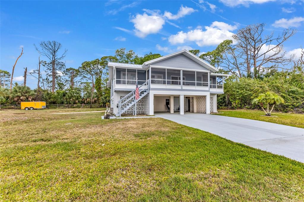 A raised, light-gray house with a screened-in porch and a concrete driveway — 3059 HOLCOMB ROAD, PORT CHARLOTTE, FL