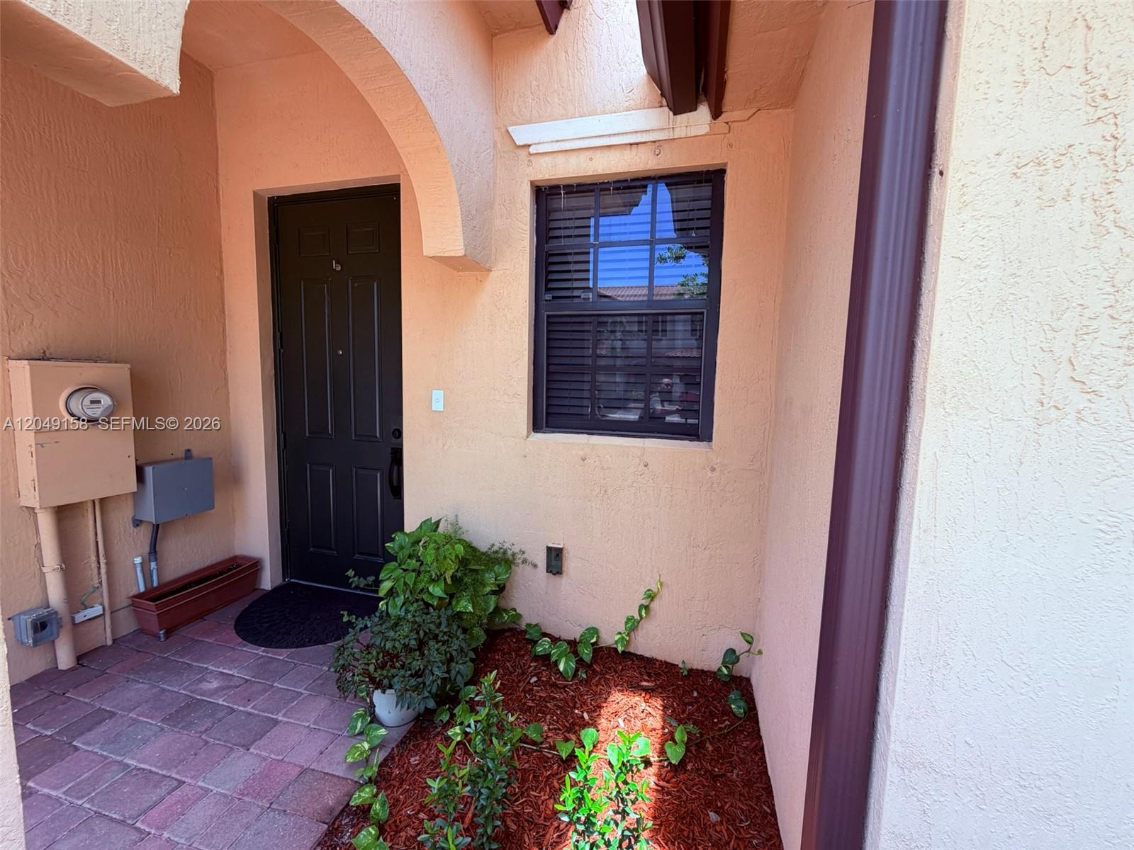 The exterior entryway features a dark door, a window with shutters, and a small garden — 3767 SE 3rd Ct, Homestead FL 33033, HOMESTEAD, FL