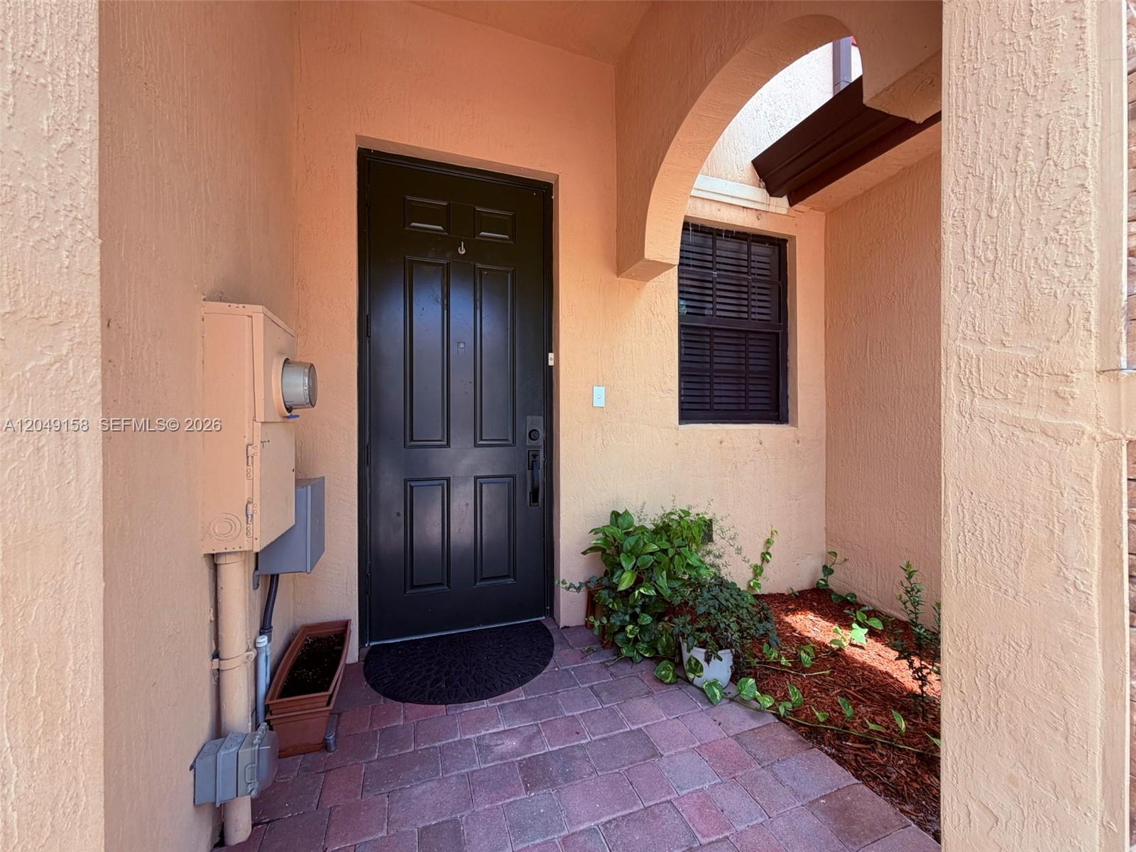 A black front door is set within a peach-colored entryway with brick pavers — 3767 SE 3rd Ct, Homestead FL 33033, HOMESTEAD, FL