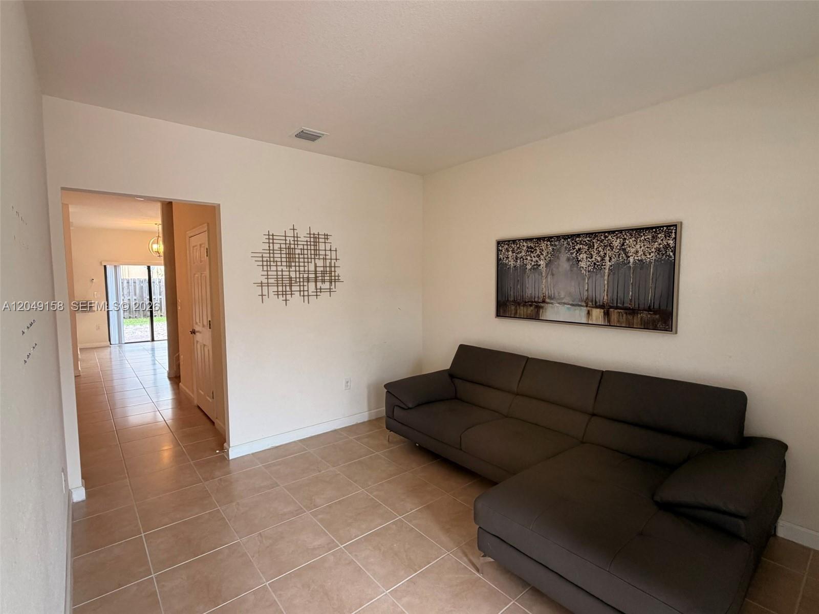 A living room features a dark gray sectional sofa, tiled floors, and wall art — 3767 SE 3rd Ct, Homestead FL 33033, HOMESTEAD, FL