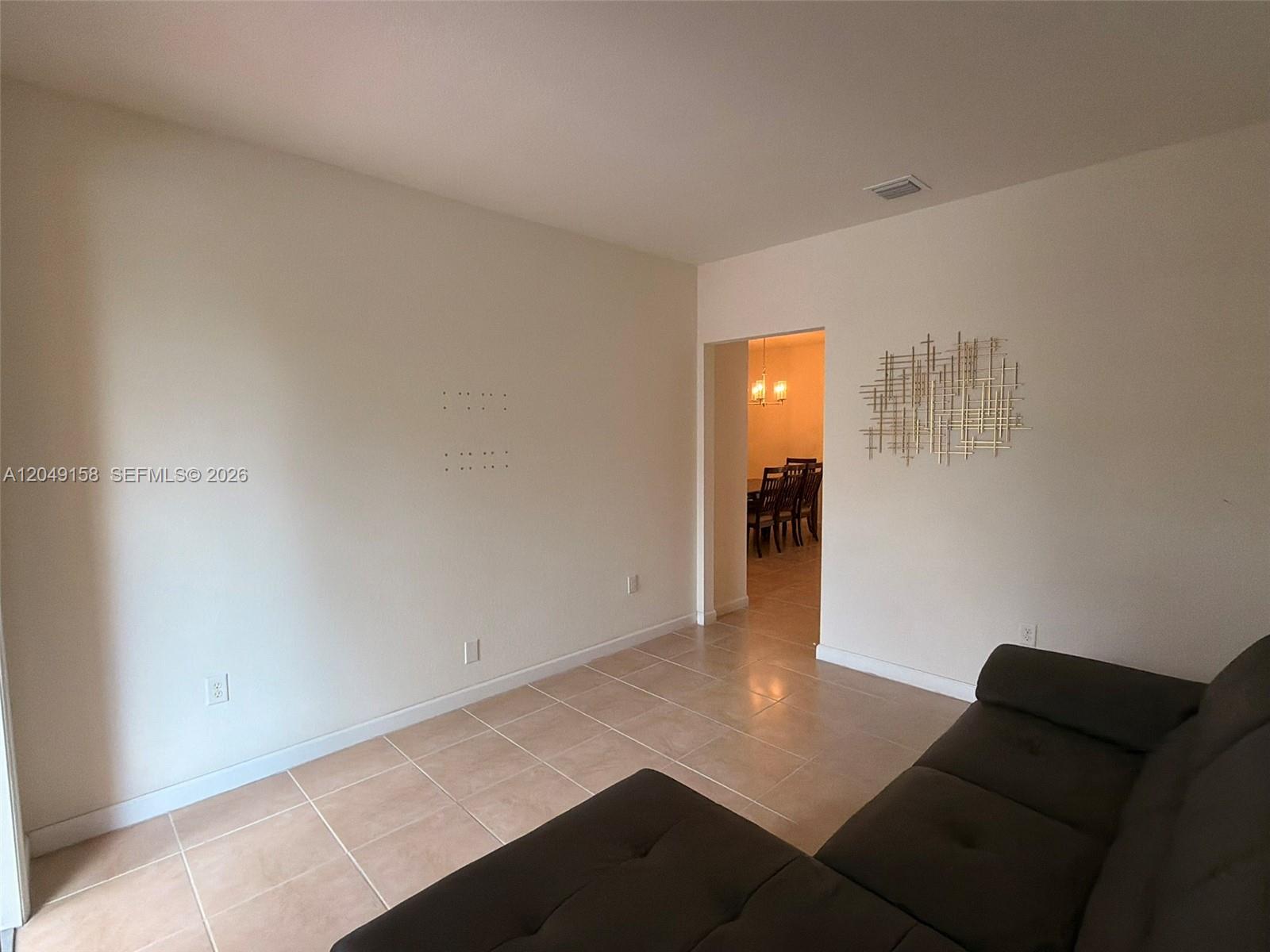 A living room features beige walls, tile flooring, a dark sofa, and wall art — 3767 SE 3rd Ct, Homestead FL 33033, HOMESTEAD, FL