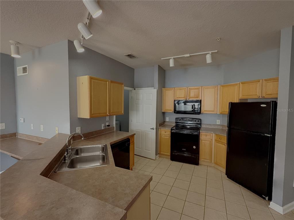 A kitchen features light wood cabinets, black appliances, a double sink, and tile flooring — 204 TERRACE RIDGE CIRCLE UNIT 204, DAVENPORT, FL