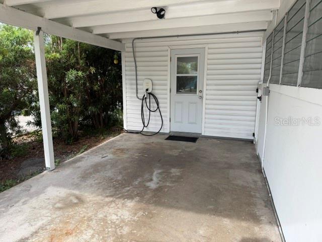 A covered concrete carport features a white door and an electric vehicle charging station — 1205 PRINCETON AVENUE, BRADENTON, FL