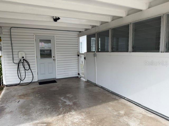 A covered carport features a white door, concrete flooring, and an electric vehicle charger — 1205 PRINCETON AVENUE, BRADENTON, FL