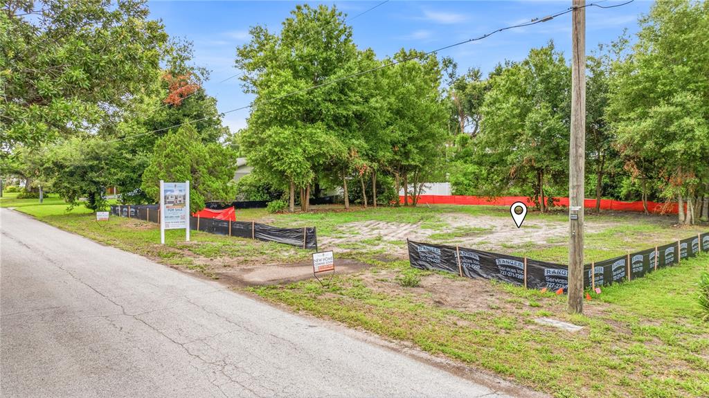 A vacant, fenced-in residential lot sits beside a paved road with trees in the background — 1008 W ADALEE STREET, TAMPA, FL