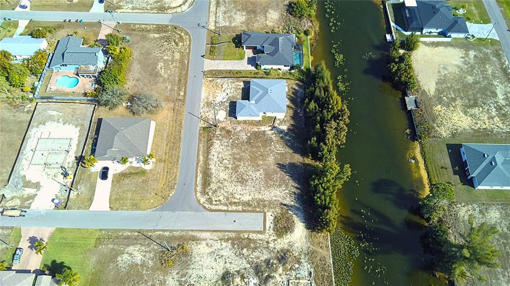 An aerial view shows several suburban houses, a canal, and vacant lots — 122 NE 9TH STREET, CAPE CORAL, FL