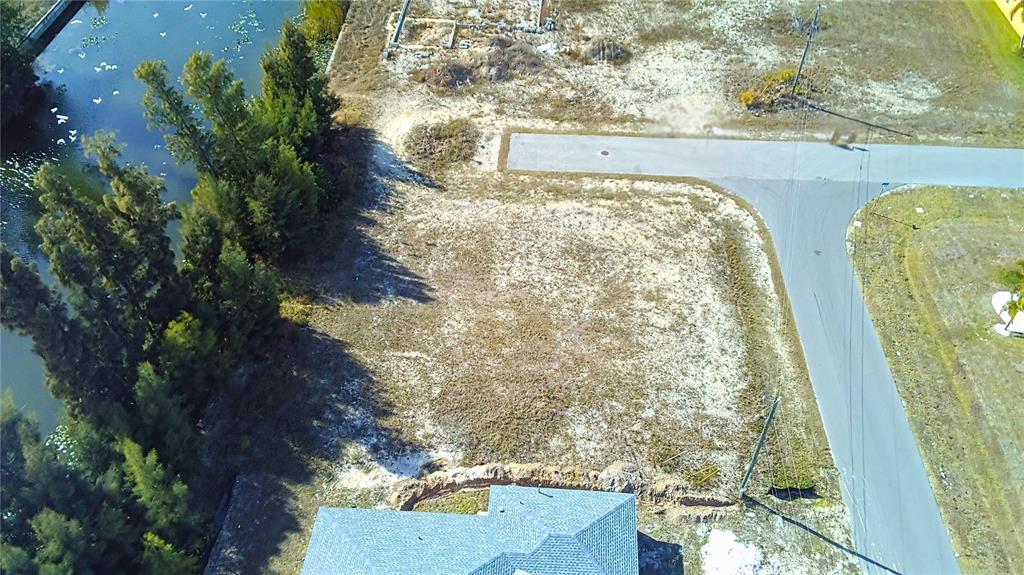 An aerial view shows a vacant residential lot next to a canal and a road — 122 NE 9TH STREET, CAPE CORAL, FL