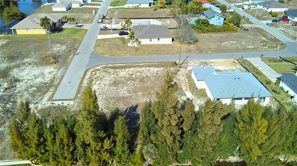 An aerial view shows a vacant residential lot situated between two houses and a road — 122 NE 9TH STREET, CAPE CORAL, FL