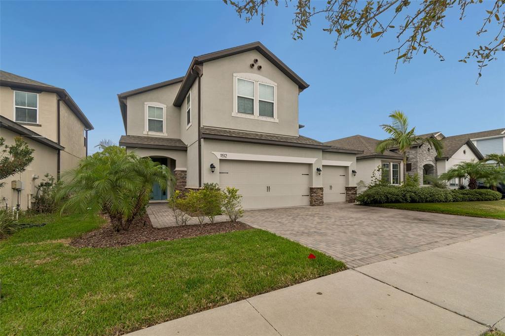 A paved walkway leads to a blue front door framed by stone pillars and siding — 11512 NAVEL ORANGE WAY, TAMPA, FL