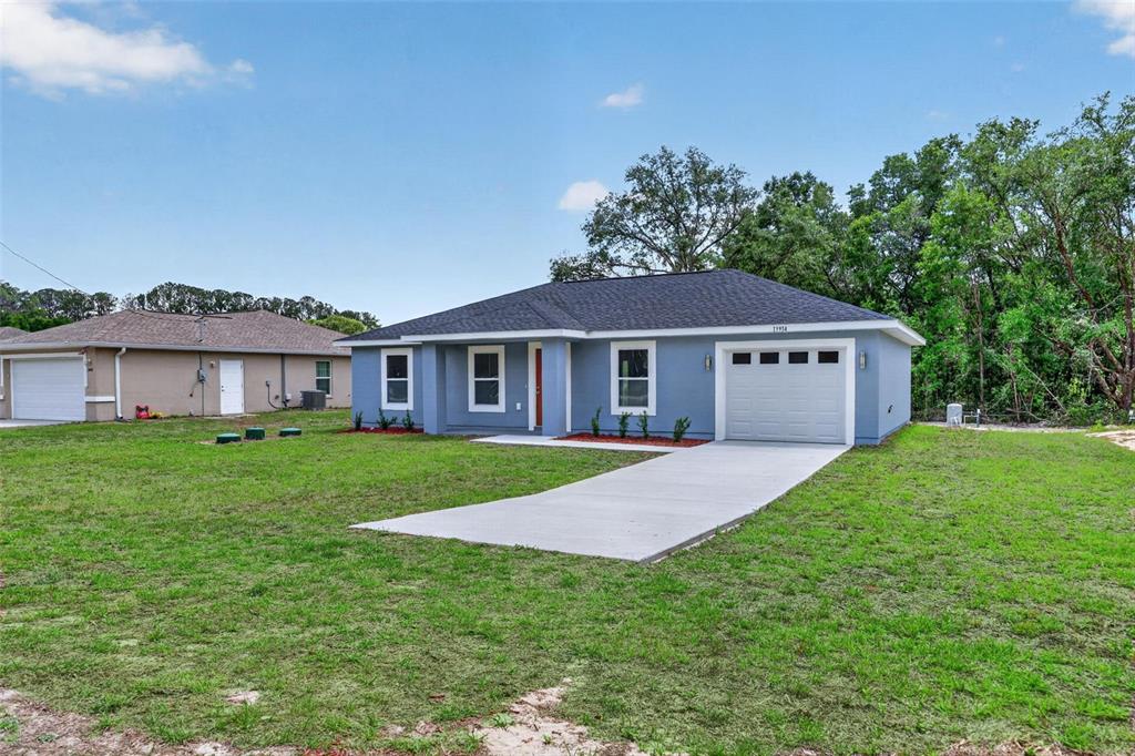 A blue single-story house with a white garage door and a concrete driveway — 13914 SW 104TH LANE, DUNNELLON, FL