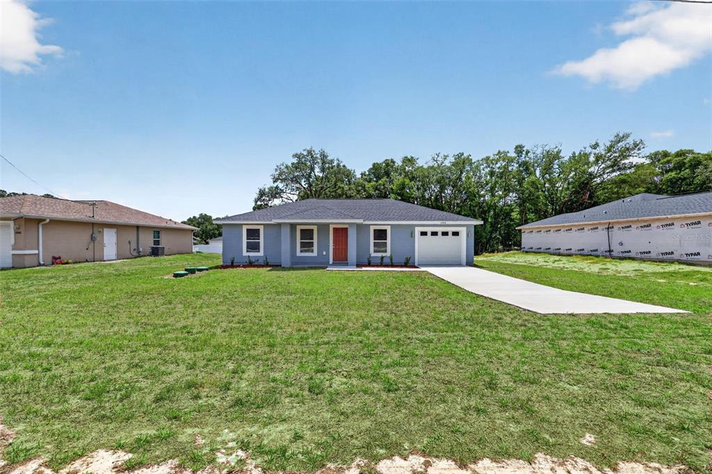 A newly constructed single-story house with a gray exterior, a garage, and a front lawn — 13914 SW 104TH LANE, DUNNELLON, FL