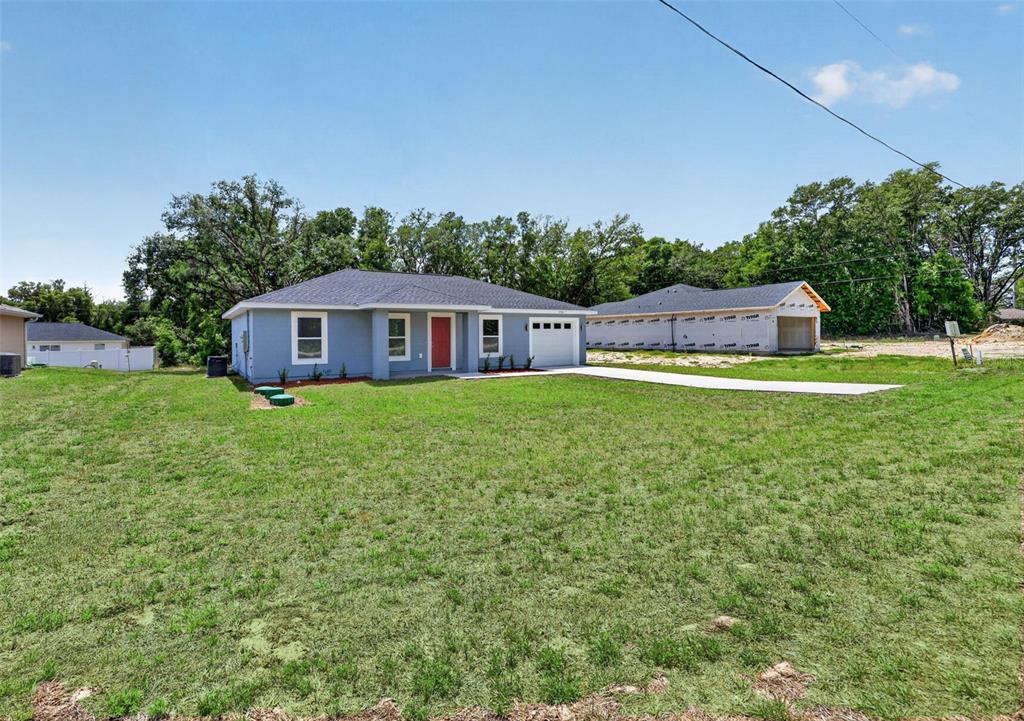 A blue single-story house with a red front door stands next to a construction site — 13914 SW 104TH LANE, DUNNELLON, FL