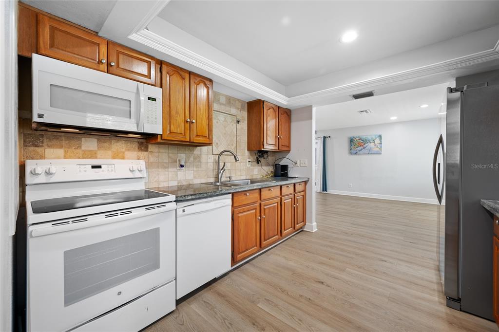 A kitchen features wood cabinets, white appliances, granite countertops, and light wood-look flooring — 4115 55TH AVENUE DRIVE E, BRADENTON, FL