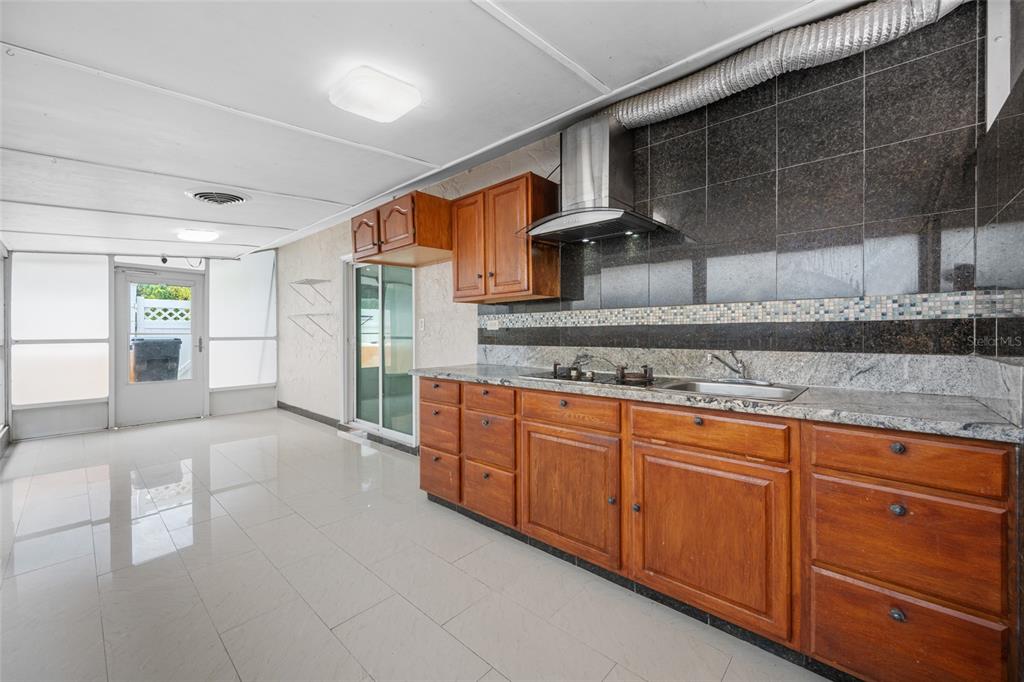 A kitchen with wood cabinets, granite countertops, and dark tile walls in a sunroom area — 4115 55TH AVENUE DRIVE E, BRADENTON, FL