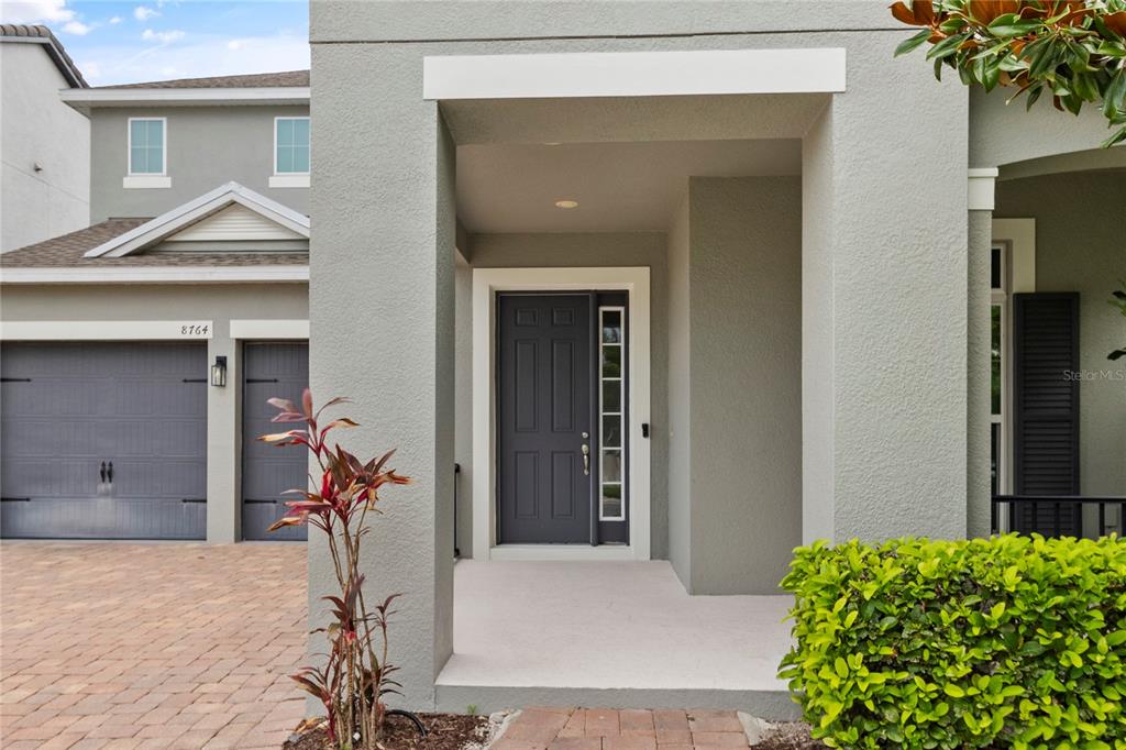 The exterior of a gray house features a covered entryway with a dark front door — 8764 POWDER RIDGE TRAIL, WINDERMERE, FL