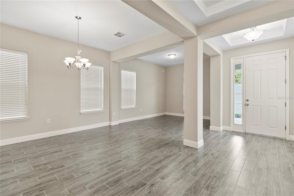An open-concept room features gray wood-look tile flooring, neutral walls, and a white front door — 8764 POWDER RIDGE TRAIL, WINDERMERE, FL