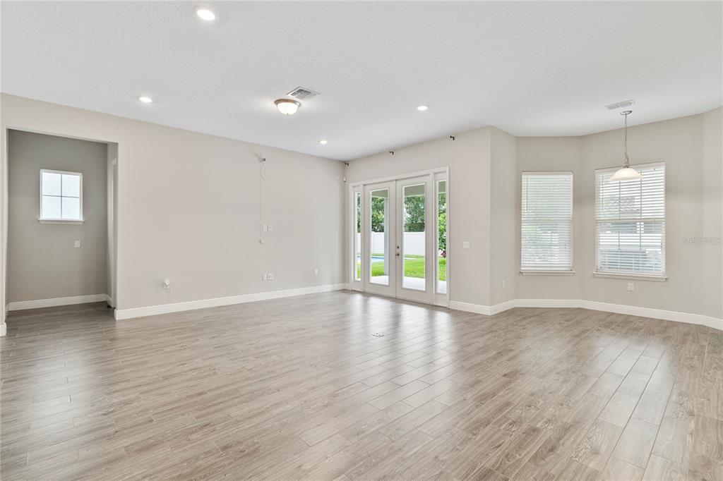 An empty living room with light wood-look tile flooring, neutral walls, and glass patio doors — 8764 POWDER RIDGE TRAIL, WINDERMERE, FL
