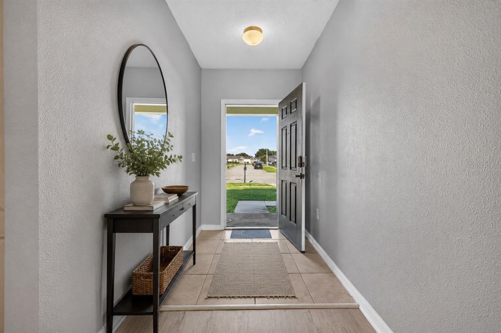 An entryway features a console table, an oval mirror, tile flooring, and an open front door — 573 LUCERNE BOULEVARD, WINTER HAVEN, FL