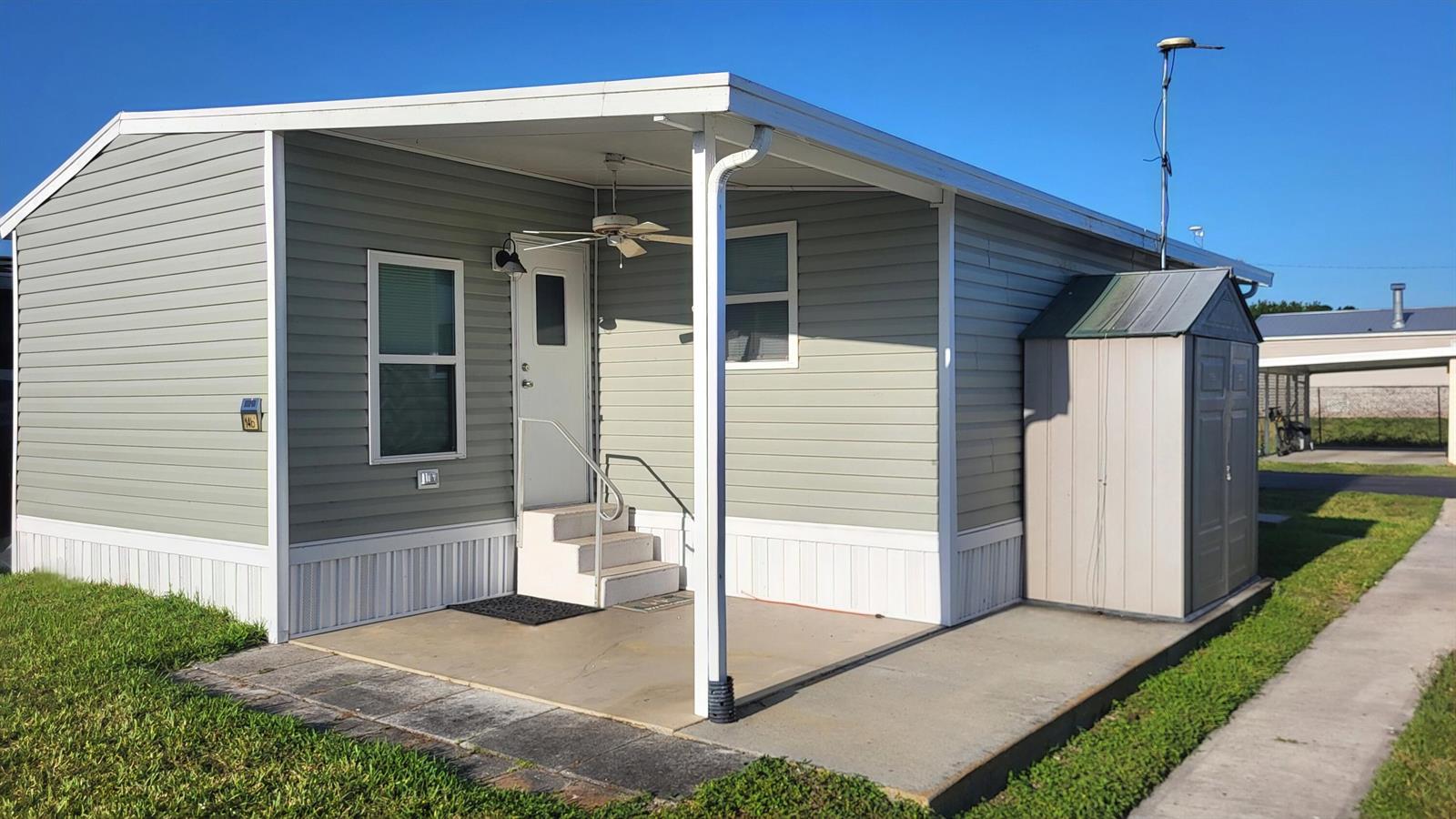 A light green mobile home with a covered concrete patio, stairs, and an outdoor shed — 1339 Old Lakeport Road # 14b, Moore Haven FL 33471, MOORE HAVEN, FL
