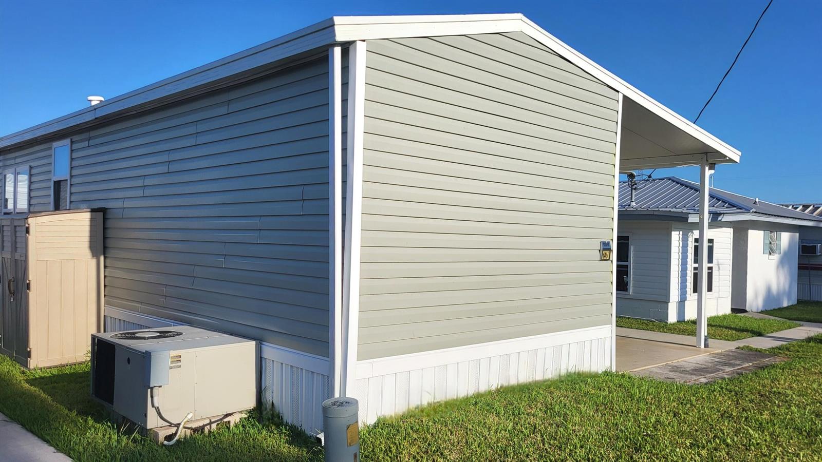 The exterior of a light green manufactured home features white trim, a carport, and an AC unit — 1339 Old Lakeport Road # 14b, Moore Haven FL 33471, MOORE HAVEN, FL