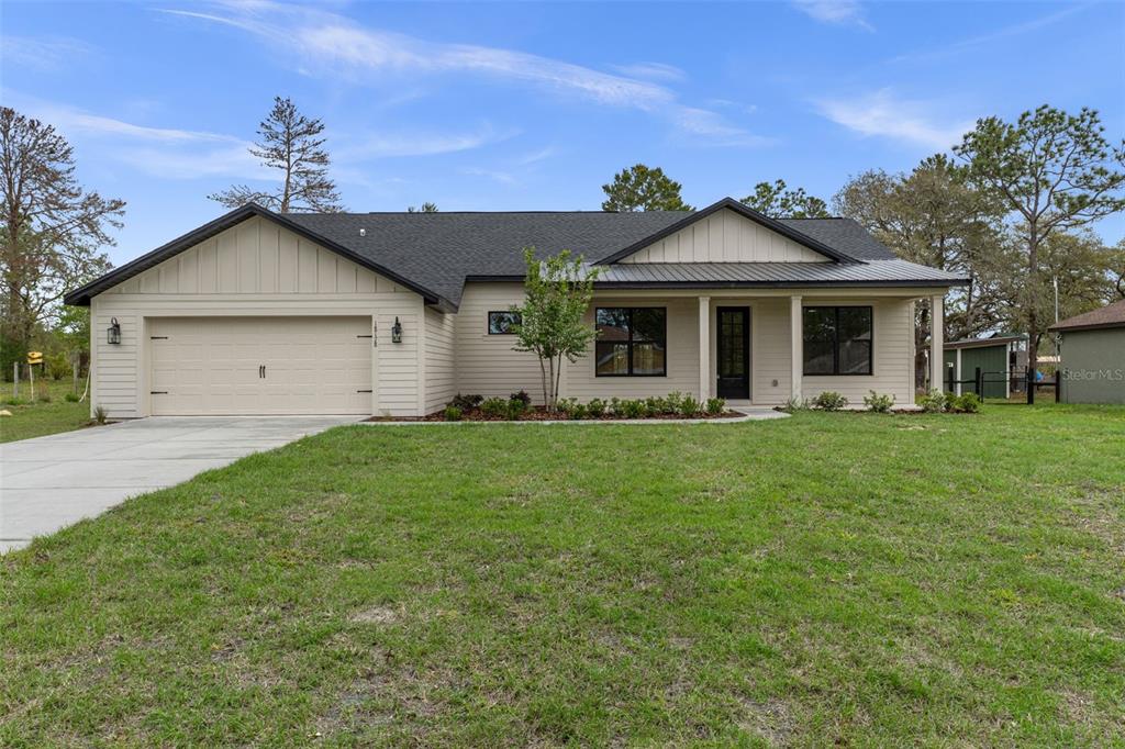 A single-story house with beige siding, a dark metal roof, and a two-car garage — 18178 MABERLY ROAD, WEEKI WACHEE, FL