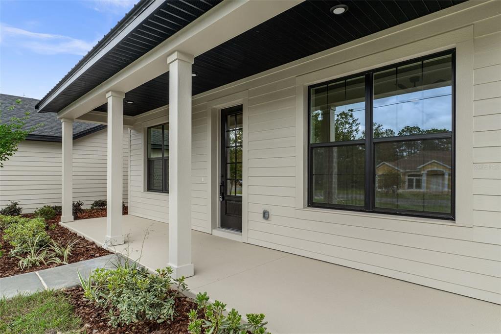 A covered front porch features white siding, black window frames, and a dark entry door — 18178 MABERLY ROAD, WEEKI WACHEE, FL