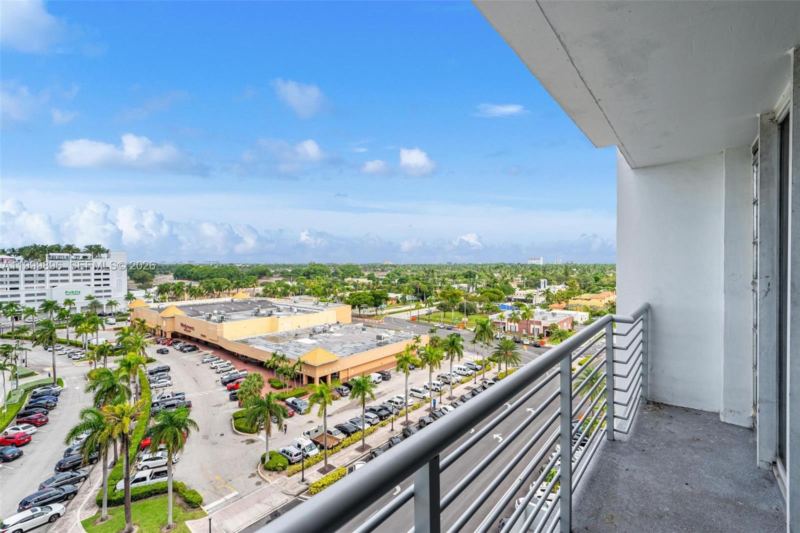 A high-angle view from a balcony overlooking a parking lot, shopping center, and surrounding landscape — 1720 Harrison St # 9F, Hollywood FL 33020, HOLLYWOOD, FL