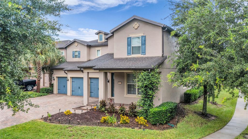 A two-story tan stucco house features blue shutters, a brick driveway, and a covered entryway — 7052 ENCHANTED LAKE DRIVE, WINTER GARDEN, FL