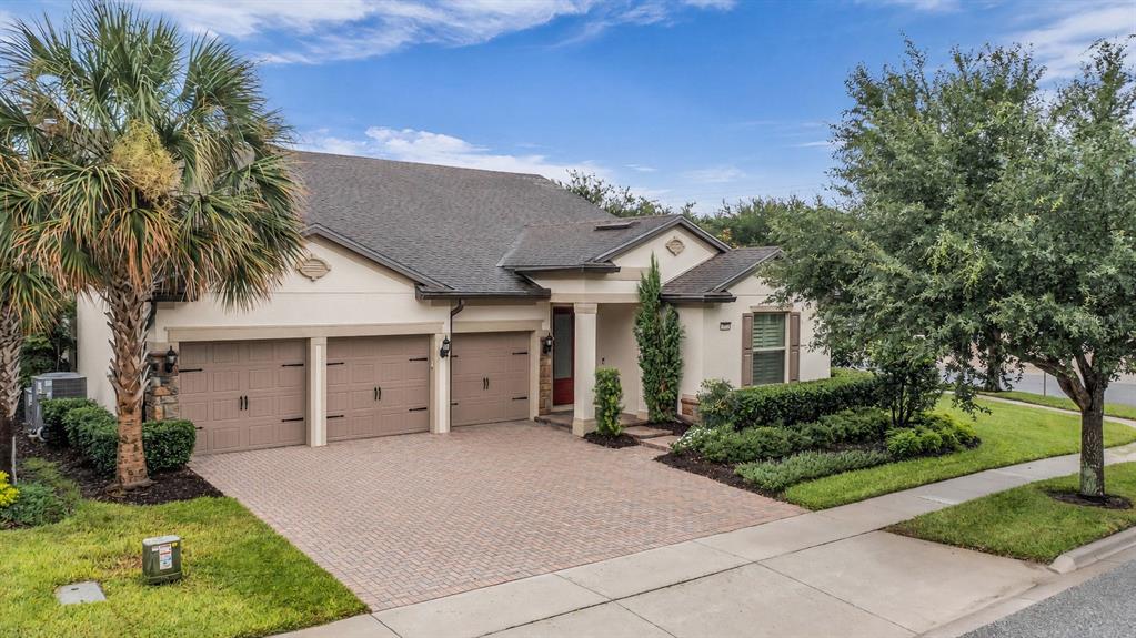 A single-story house with a three-car garage, brick paver driveway, and mature landscaping — 7052 ENCHANTED LAKE DRIVE, WINTER GARDEN, FL