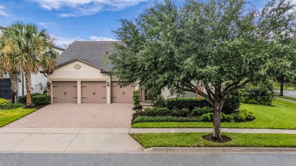 A single-story house with a three-car garage, brick paver driveway, and a large front tree — 7052 ENCHANTED LAKE DRIVE, WINTER GARDEN, FL