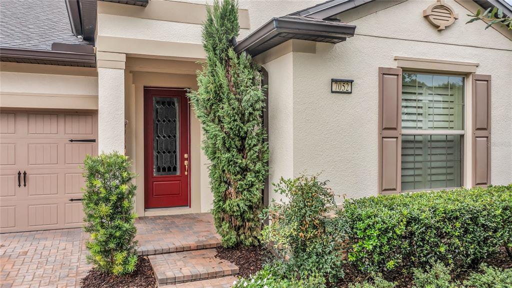 A red front door is set beside a garage and a window with brown shutters — 7052 ENCHANTED LAKE DRIVE, WINTER GARDEN, FL