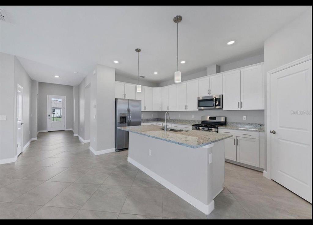 A modern kitchen features white cabinets, granite countertops, stainless steel appliances, and light tile flooring — 5127 CORAL REEF WAY, BRADENTON, FL