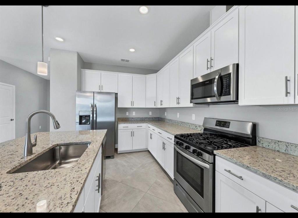A kitchen features white cabinets, granite countertops, stainless steel appliances, and a large island — 5127 CORAL REEF WAY, BRADENTON, FL