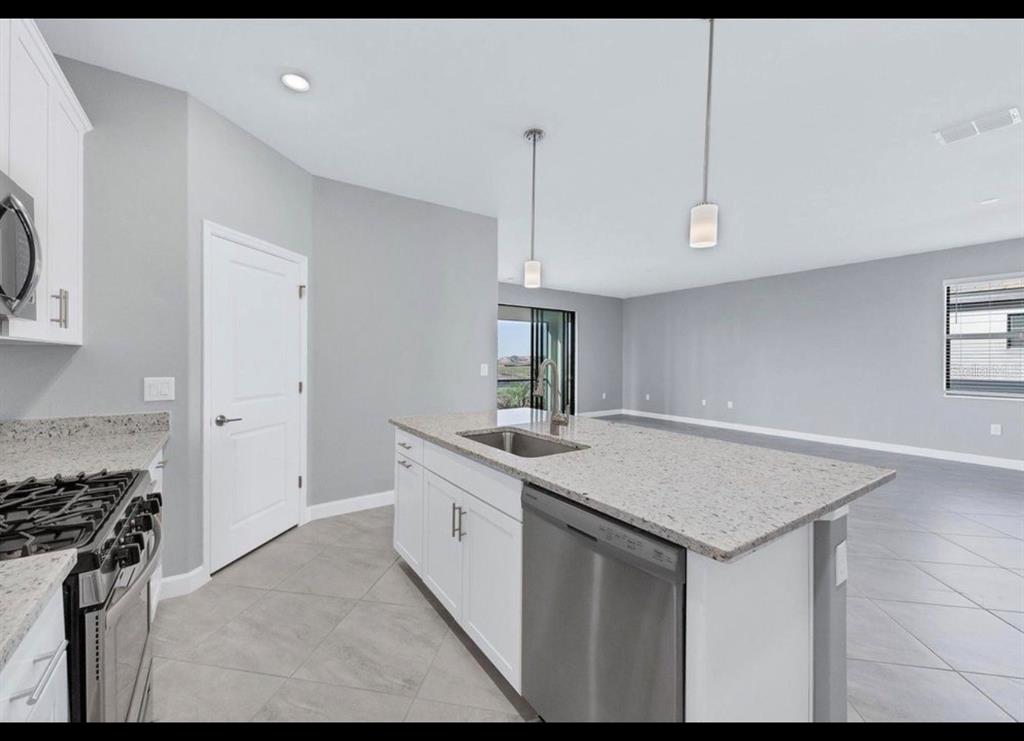 A kitchen with white cabinets, granite countertops, and a stainless steel dishwasher overlooks a living area — 5127 CORAL REEF WAY, BRADENTON, FL