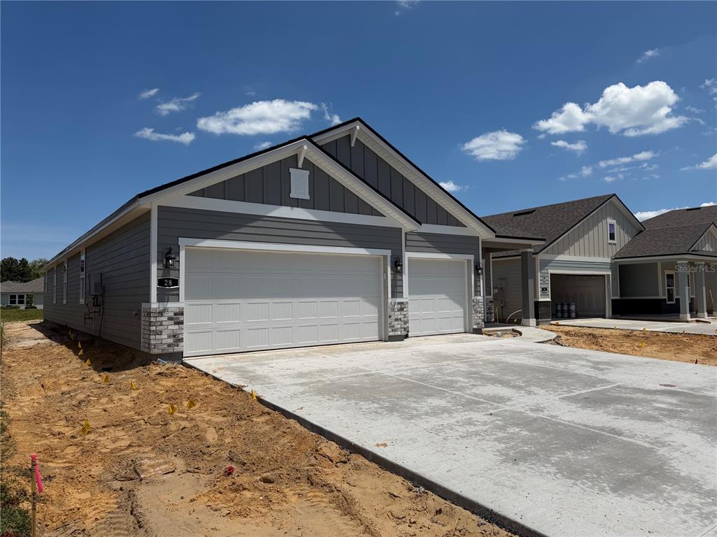 A gray-sided house with a three-car garage and stone accents stands on a dirt lot — 28 PERSEUS AVENUE, FLAGLER BEACH, FL
